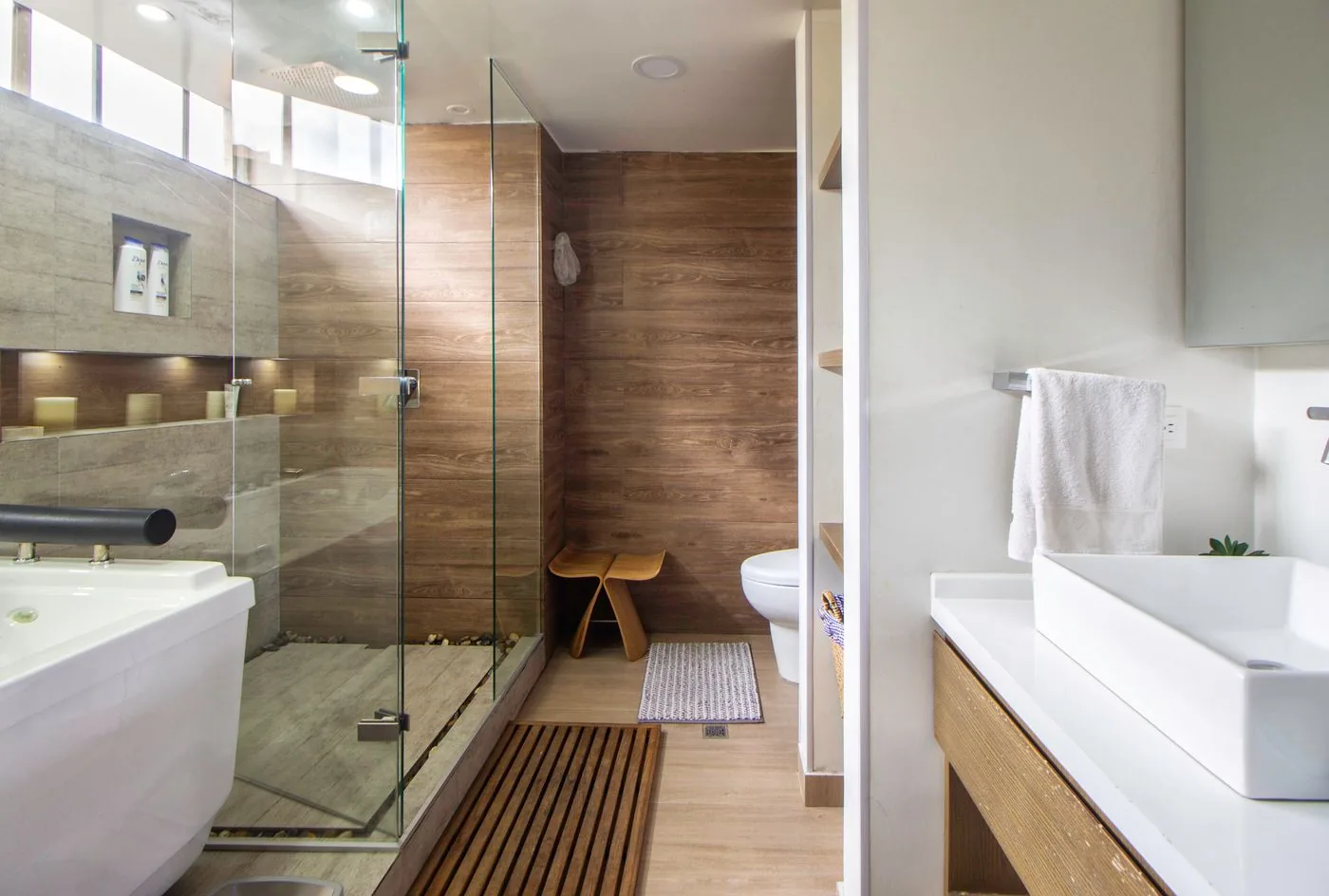 Kamar mandi bercahaya alami dengan pancuran kaca dan detail kayu