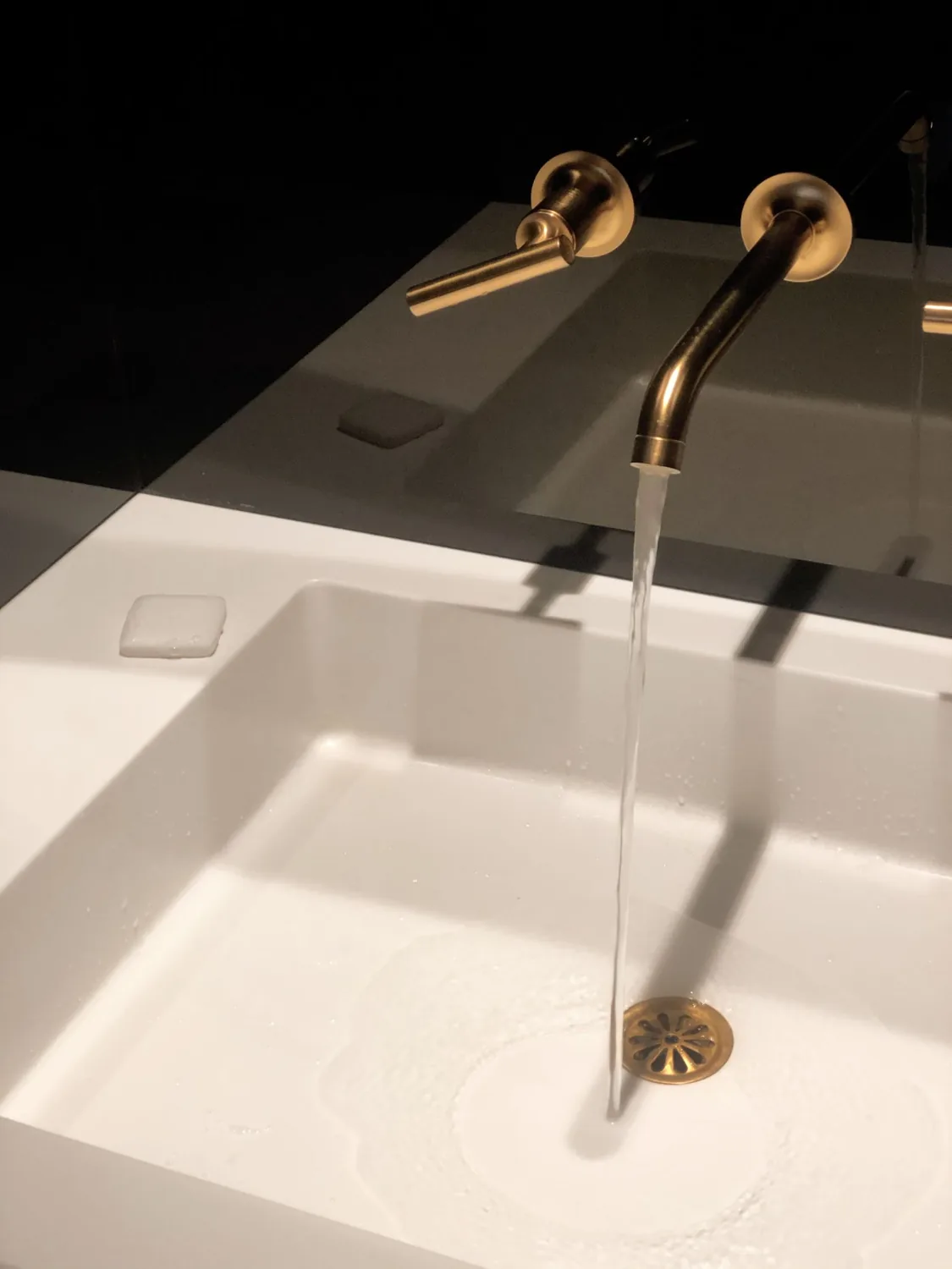 Goldfarbene Wandarmatur über einem eckigen Waschbecken